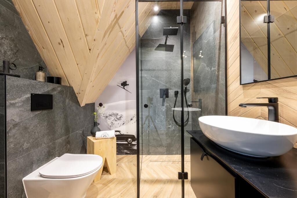 A modern bathroom with a glass shower enclosure, a white sink, and a wooden vanity.