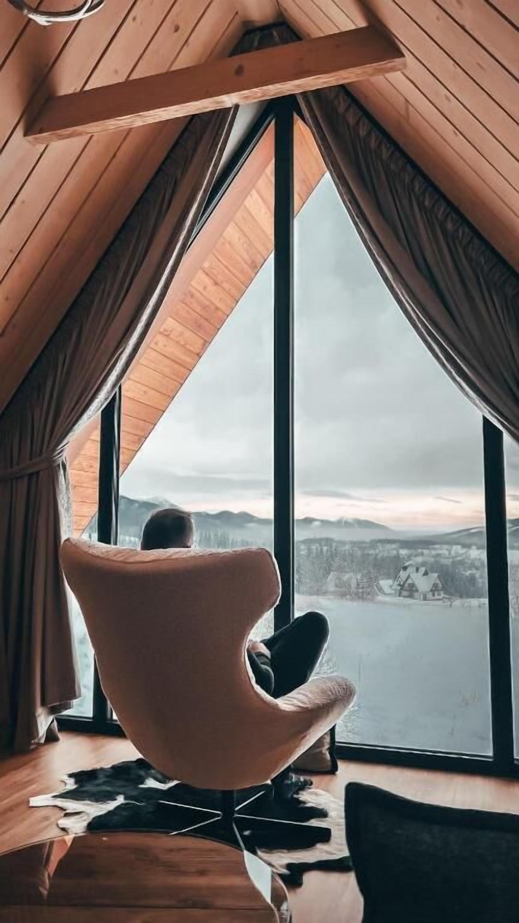 A room with a large window, a chair, and a view of a body of water.