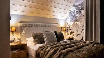 A bedroom with a wooden ceiling, a bed with a fur throw, two bedside lamps, and a wall with a mountain landscape.