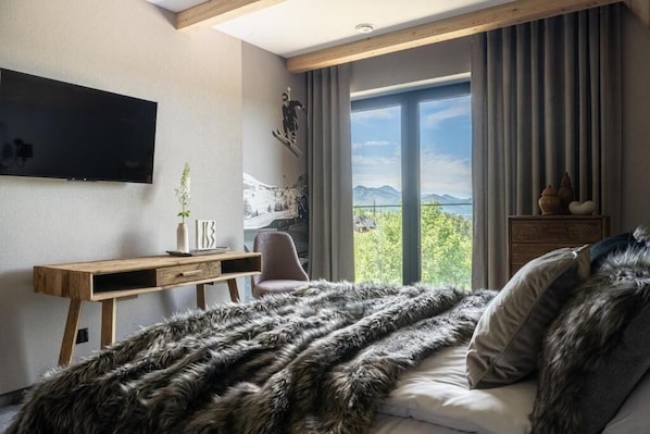 A modern bedroom with a large bed, a desk, a chair, and a TV mounted on the wall.