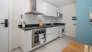 A compact kitchen with a microwave, oven, and washing machine. - Corporate Stays First Living - 505 (Asunción)