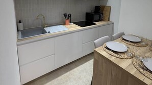 Moderni keittiö, jossa on valkoiset kaapit, musta mikroaaltouuni ja puinen ruokapöytä, jonka päällä on lautasia ja laseja.