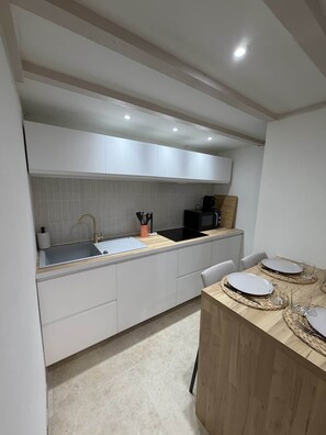 A modern kitchen with white cabinets, a black microwave, and a wooden dining table set with plates and glasses. - Le Petit Venard | Private parking | Private terrace (Vieux-Boucau-les-Bains)