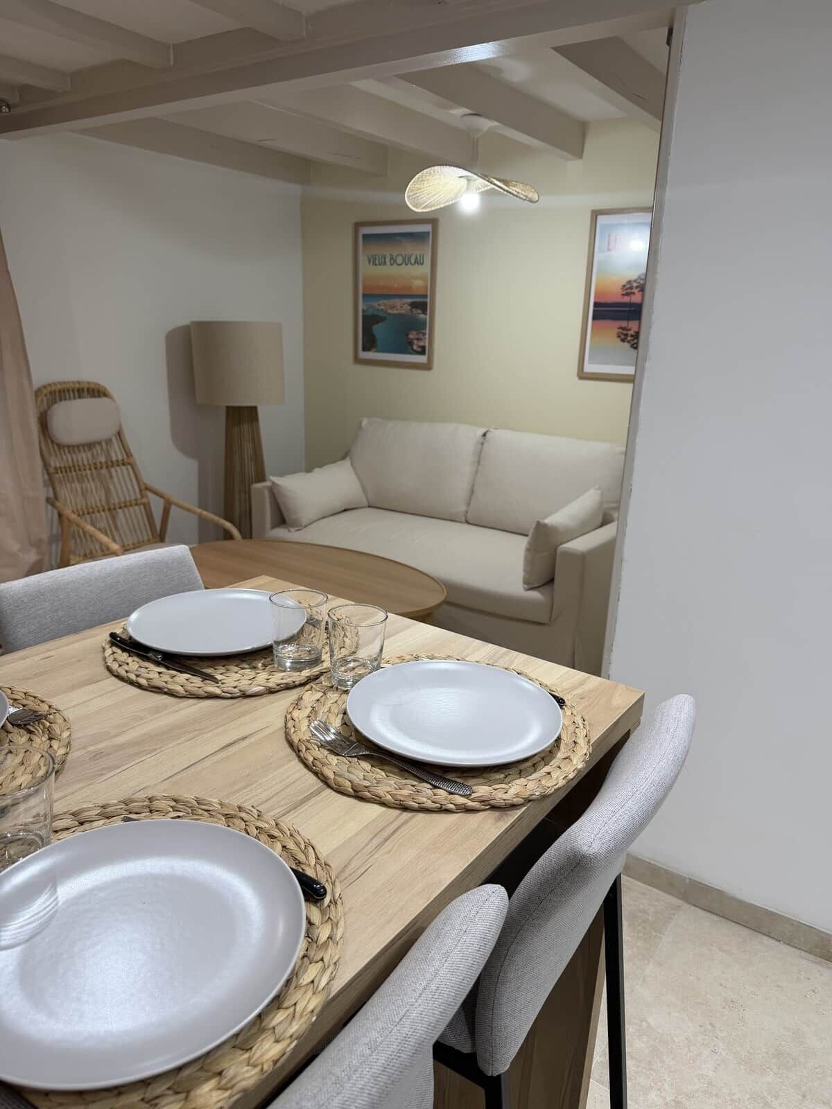 Un coin repas avec une table en bois dressée pour quatre personnes, deux chaises, un set de table en fibres tressées et un tableau encadré accroché au mur.