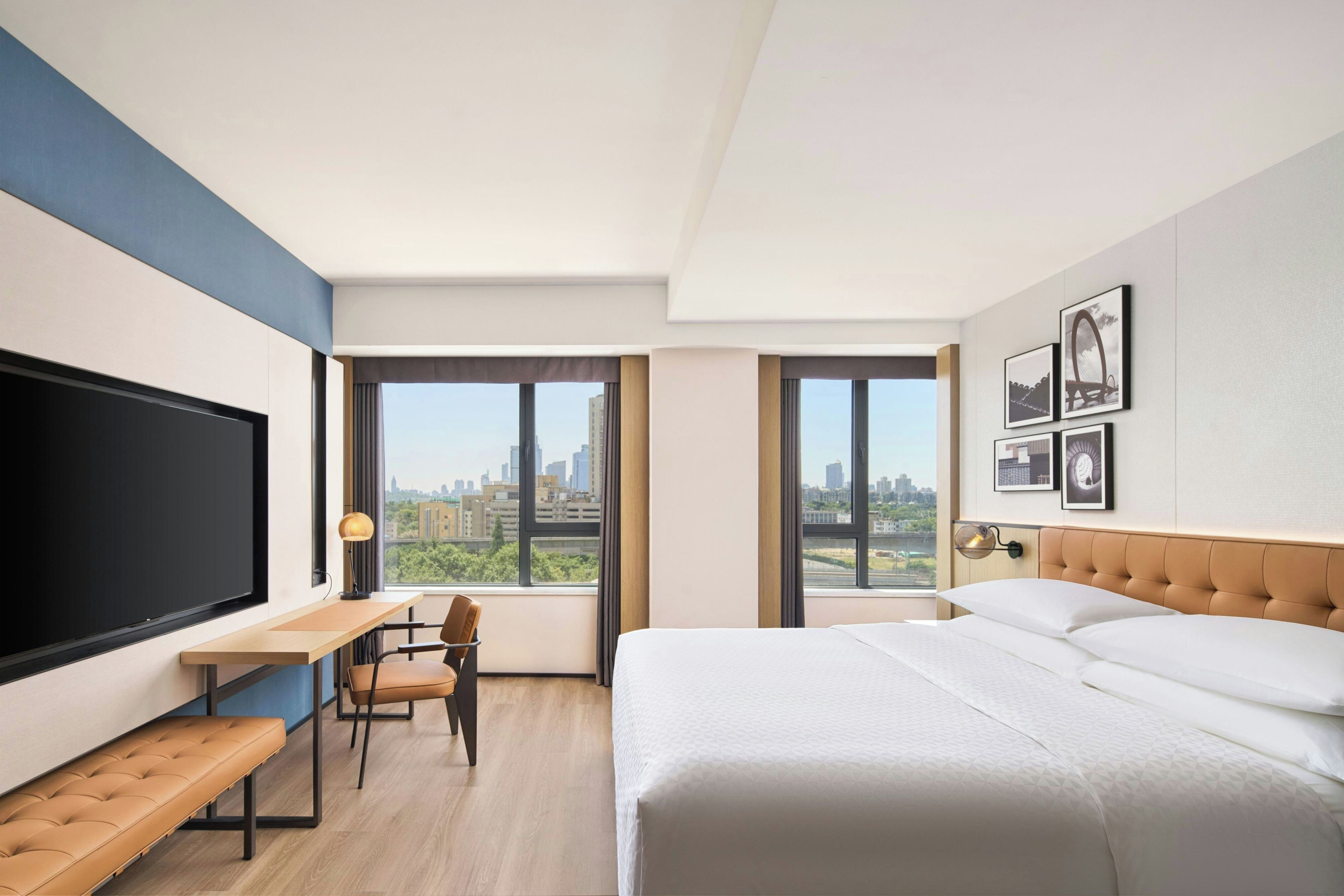 A modern hotel room with a large bed, a desk, a chair, and a TV.