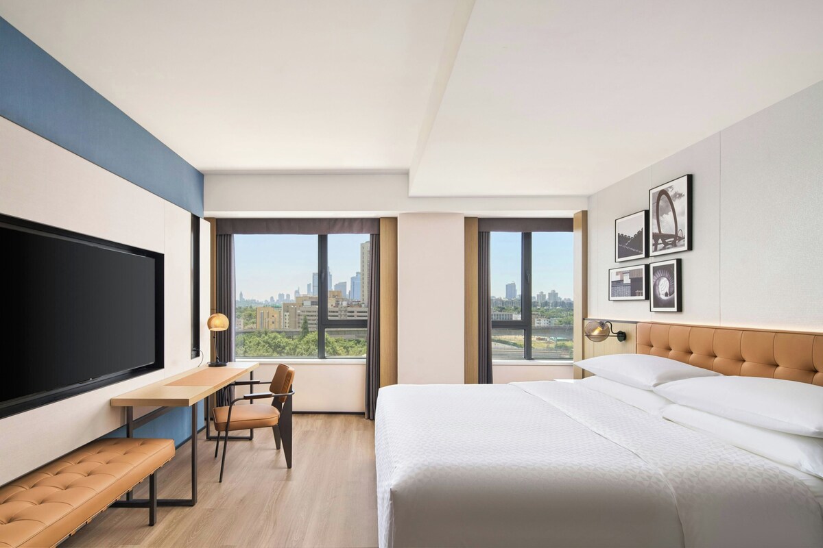 Una habitación de hotel moderna con una cama grande, un escritorio, una silla y un televisor.