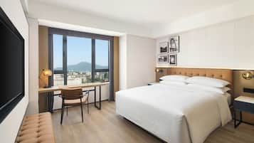Ein Hotelzimmer mit Bett, Schreibtisch, Stuhl, Fernseher und einem Fenster mit Blick auf die Stadt.