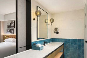Une salle de bain d’hôtel avec un grand miroir, deux lavabos, un mur recouvert de carreaux bleus et un lit avec du linge de maison blanc.