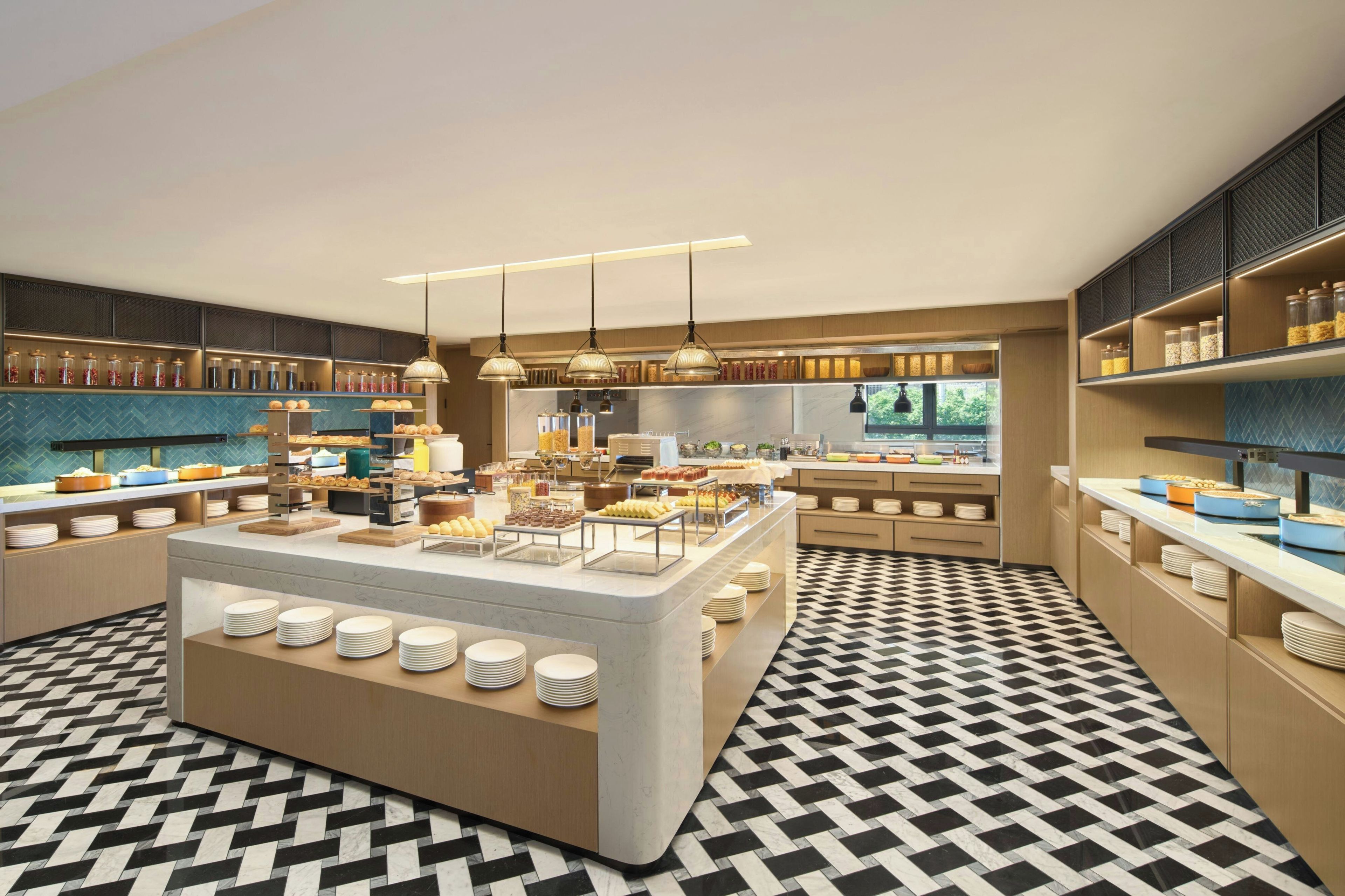 A modern breakfast buffet with a central island, multiple serving stations, and a patterned floor.