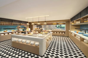 Un moderno bufé de desayuno con una isla central, varias estaciones de servicio y un piso con diseño.
