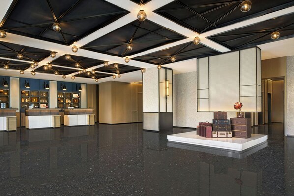 Un hall d’entrée spacieux avec un plafond haut, un décor géométrique au plafond et un espace de réception doté d’un comptoir et d’étagères.