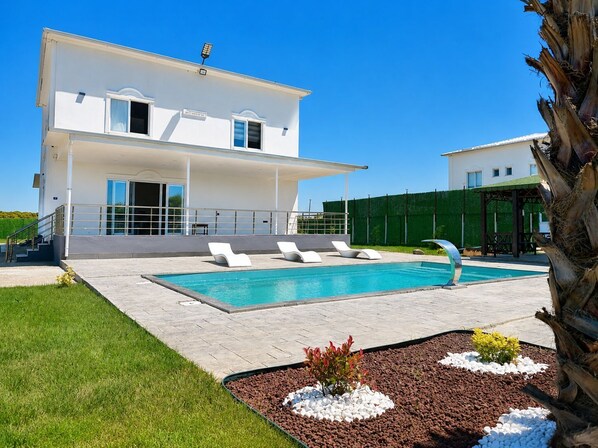 Una casa moderna de dos pisos con piscina, mobiliario de exterior y un jardín cuidado.