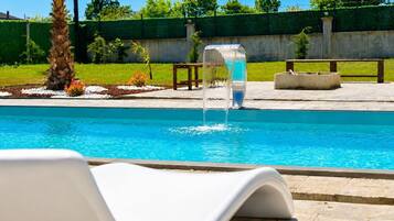 A swimming pool with a water feature, surrounded by a garden with a palm tree and benches.