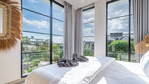 Ein Schlafzimmer mit einem großen Bett, Blick auf Grünflächen und Gebäude, und einem modernen Design.