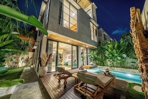Uma casa moderna de dois andares com piscina, área de estar externa e vegetação exuberante.