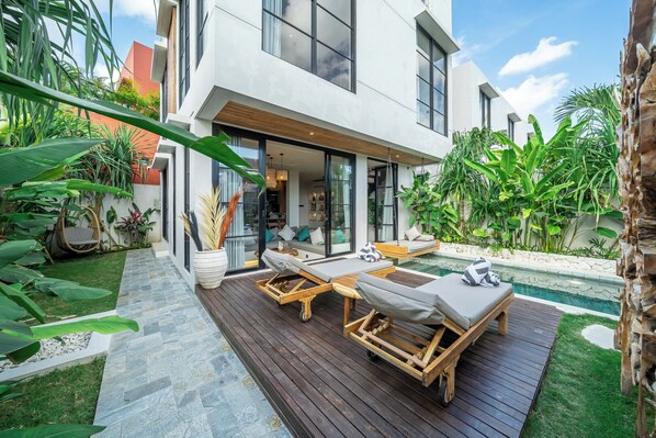 Una casa moderna con piscina, sillas de descanso y jardín.