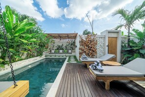 Zona junto a la piscina con terraza de madera, sillones de descanso y un área de estar con cojines.