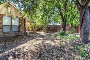 A backyard with a brick house, a wooden deck, and a fenced area.