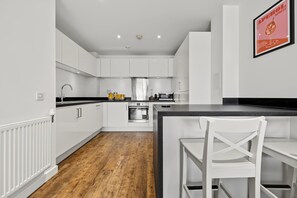 A modern kitchen with white cabinets, a wooden floor, and a black countertop. - Modern 2-Bed Flat with Balcony near Canary Wharf (London)