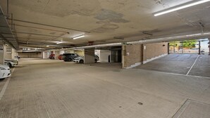 A multi-level parking garage with concrete floors and walls, several parked cars, and overhead fluorescent lighting. - Modern 2-Bed Flat with Balcony near Canary Wharf (London)