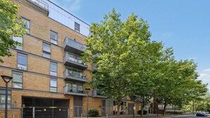 A multi-story building with a brick facade, balconies, and a tree in front. - Modern 2-Bed Flat with Balcony near Canary Wharf (London)