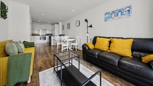A modern living room with a black leather sofa, a yellow armchair, and a glass coffee table. - Modern 2-Bed Flat with Balcony near Canary Wharf (London)