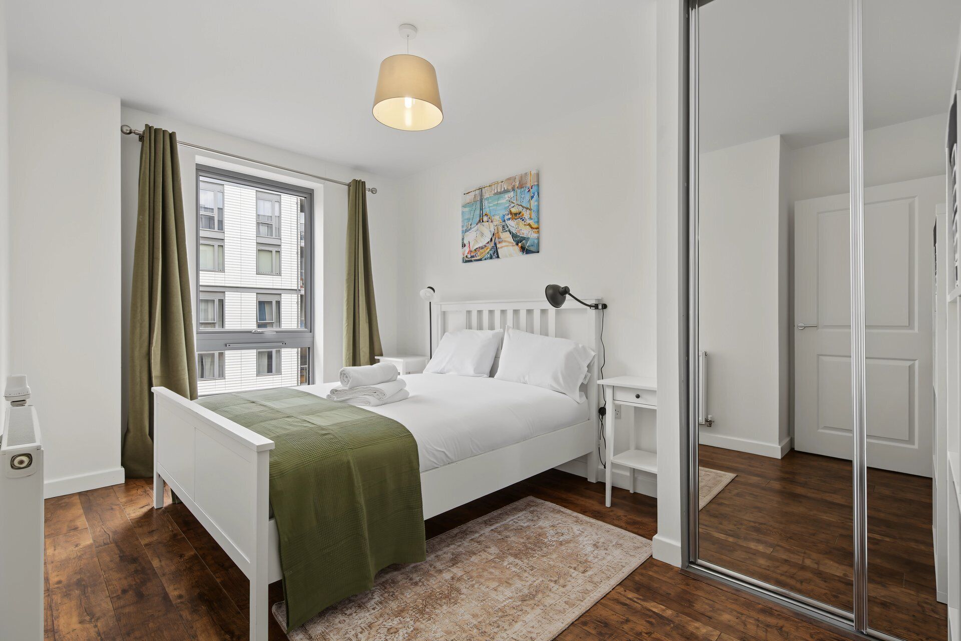 A bedroom with a bed, bedside tables, a window with curtains, a painting, and a mirror.