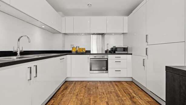 A modern kitchen with white cabinetry, a stainless steel oven, and a black countertop. - Modern 2-Bed Flat with Balcony near Canary Wharf (London)