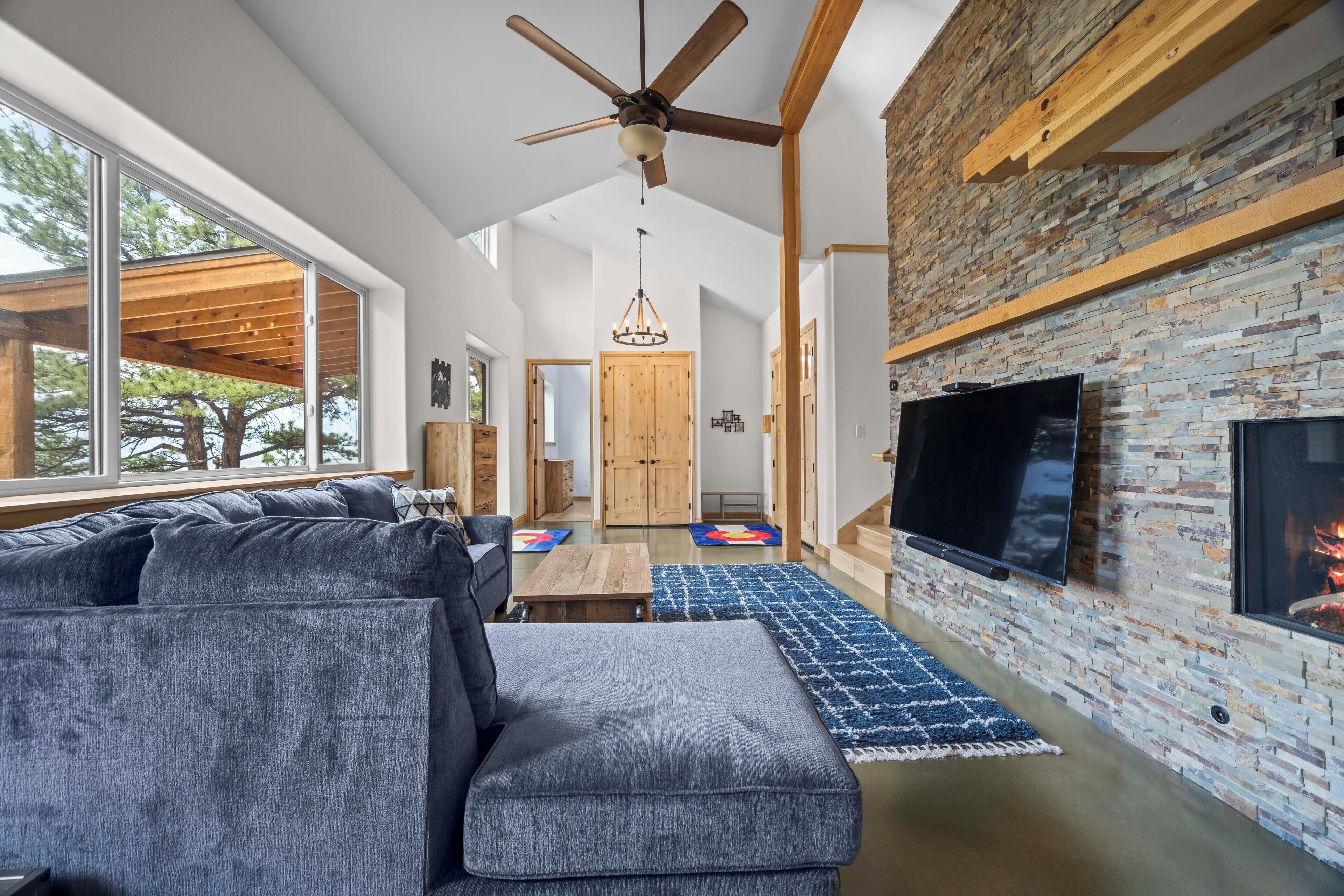 A modern living room with a sectional sofa, a fireplace, a flat-screen TV, and a ceiling fan.