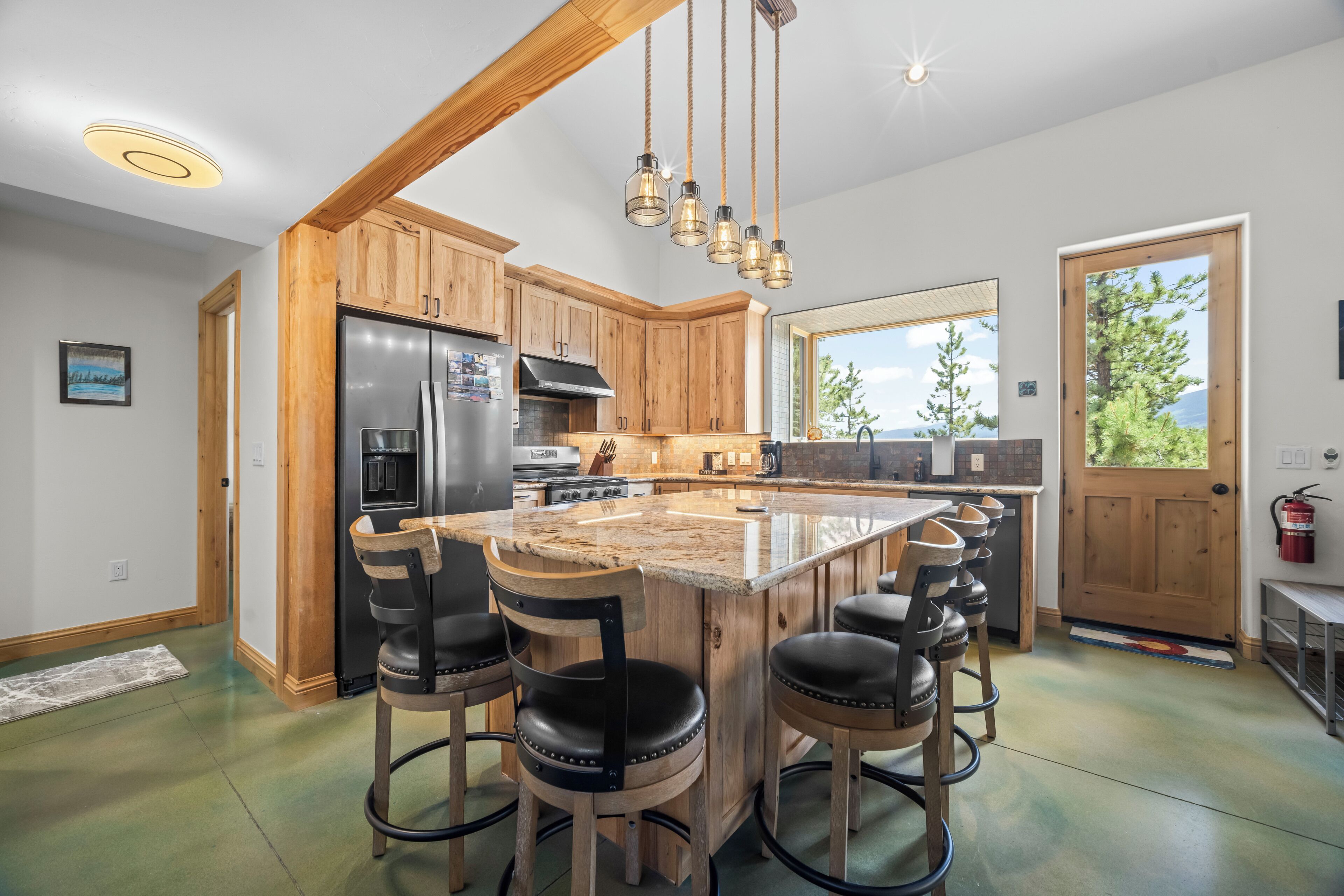 A kitchen with wooden cabinets, a stainless steel refrigerator, a large island with bar stools, and hanging pendant lights.