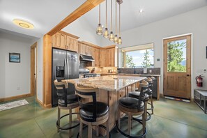 Una cocina con armarios de madera, un refrigerador de acero inoxidable, una isla grande con taburetes de bar y lámparas colgantes.