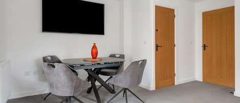 A dining area with a table, chairs, a television mounted on the wall, and wooden doors.