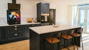 A modern kitchen with a central island, black cabinetry, and a large window. - Modern 2-Bed House Near Central Canals & Arena (Birmingham)