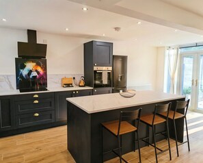 A modern kitchen with a central island, black cabinetry, and a large window. - Modern 2-Bed House Near Central Canals & Arena (Birmingham)