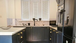 A kitchen with dark cabinets, a stainless steel refrigerator, and a window with blinds. - Modern 2-Bed House Near Central Canals & Arena (Birmingham)