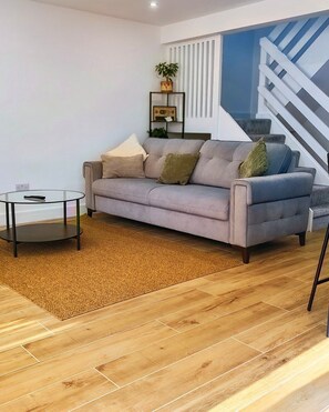 A modern living room with a grey sofa, a glass coffee table, and a wooden floor. - Modern 2-Bed House Near Central Canals & Arena (Birmingham)