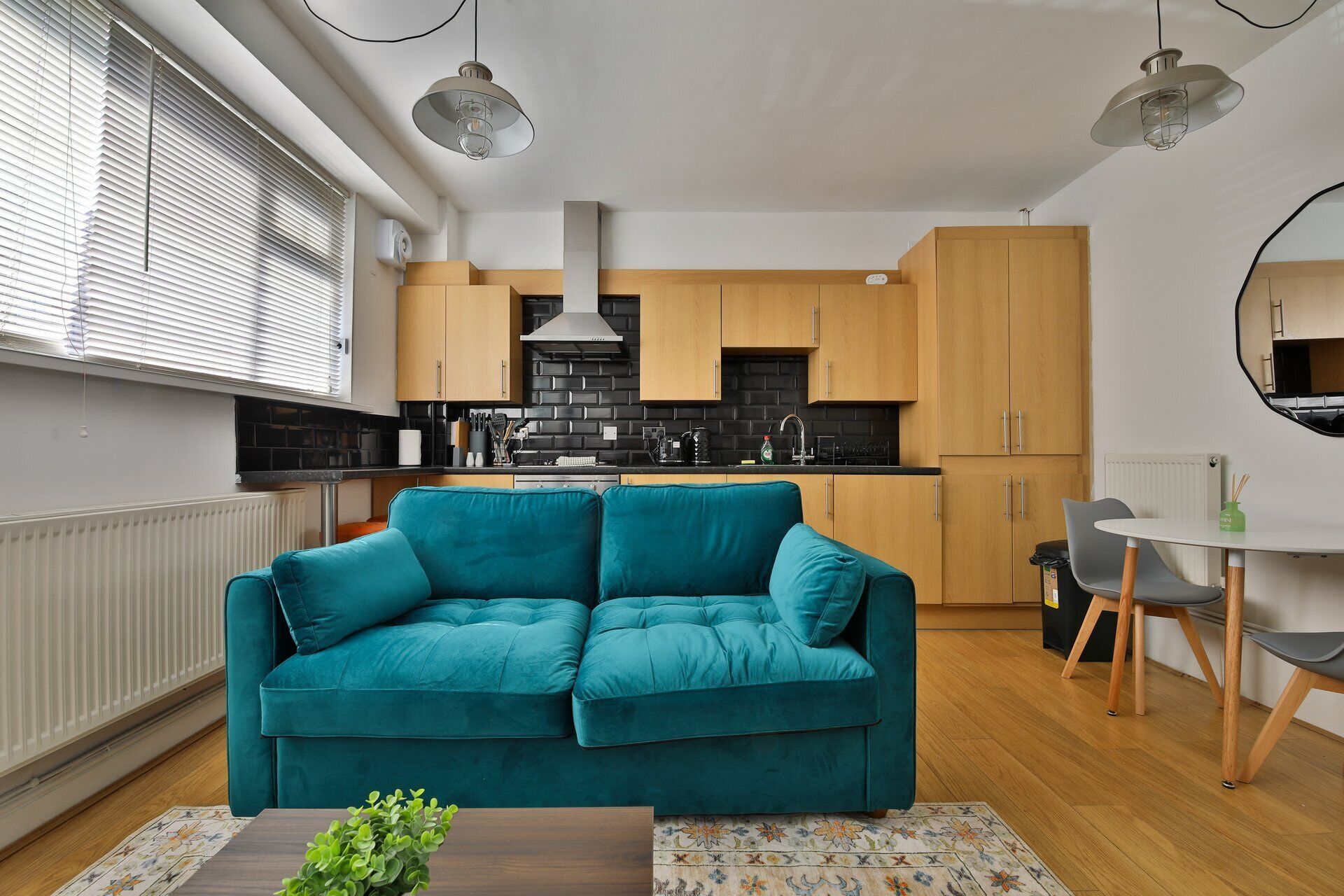 Une cuisine moderne avec des meubles de couleur noire et en bois, un îlot central et un canapé turquoise dans l’espace salon.