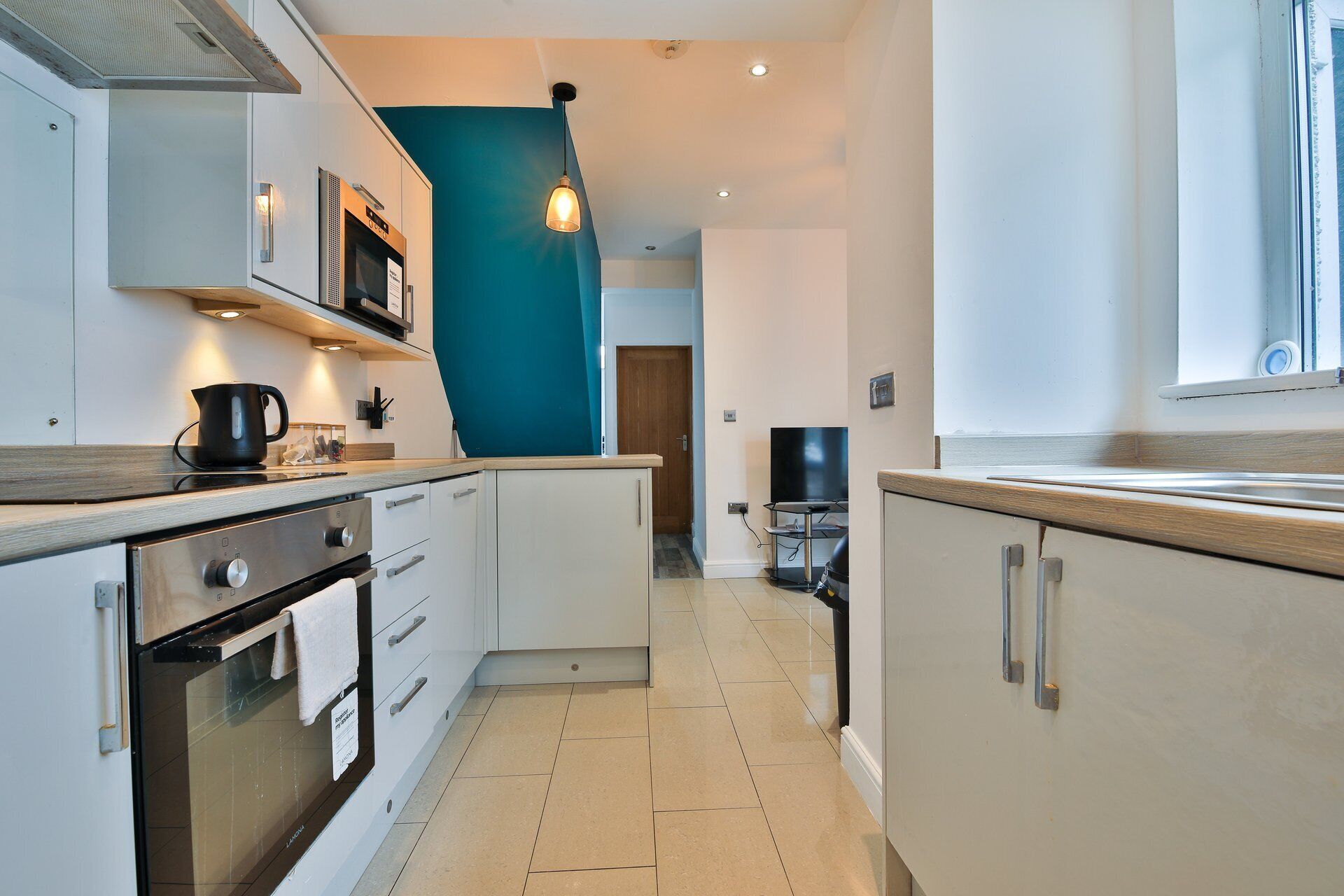 A compact kitchen with a stove, oven, microwave, and a hanging light fixture.