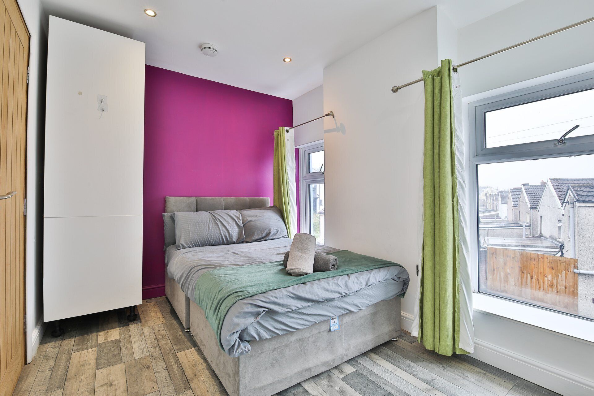 A bedroom with a bed, a wardrobe, a window with curtains, and a view of the outside.
