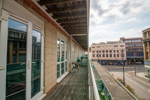 Ein Balkon mit Blick auf eine Straße, ein Gebäude mit der Aufschrift 'MUSE OF HOLES' und ein klarer Himmel.