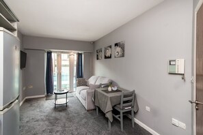 Een knus woongedeelte met een kitchenette, een bank, een eettafel en een klein rond tafeltje.
