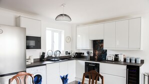 Una cocina moderna con armarios blancos, un microondas Bosch, un fregadero y una zona de comedor con una mesa dispuesta para dos personas.