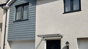 Un edificio residencial de dos pisos con garaje, una puerta principal negra y dos macetas.