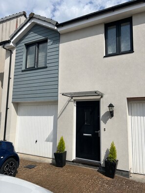 Ein zweistöckiges Wohnhaus mit Garage, einer schwarzen Haustür und zwei Blumentöpfen.