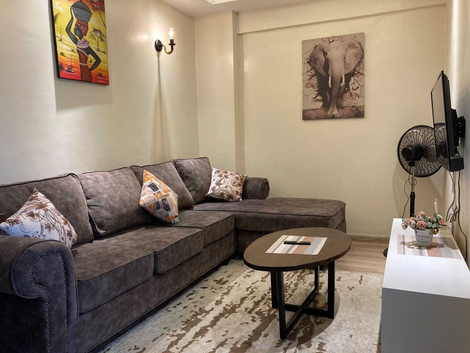 Una sala de estar con un sofá modular, una mesa de centro redonda, un ventilador de pared y dos obras de arte.