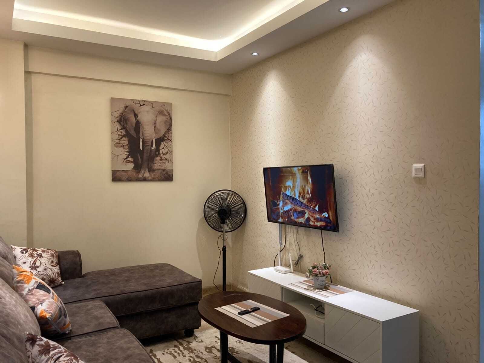 Una sala de estar moderna con un sofá, una mesa de centro, un televisor montado en la pared y un ventilador.
