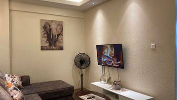 Una sala de estar moderna con un sofá, una mesa de centro, un televisor montado en la pared y un ventilador.