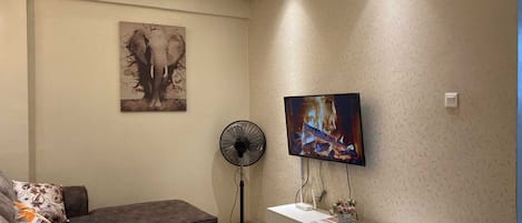 Un salon moderne avec un canapé, une table basse, un téléviseur fixé au mur et un ventilateur.