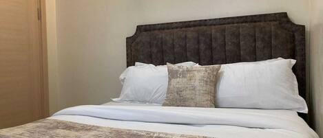 Una cama con cabecera, almohadas y una colcha.