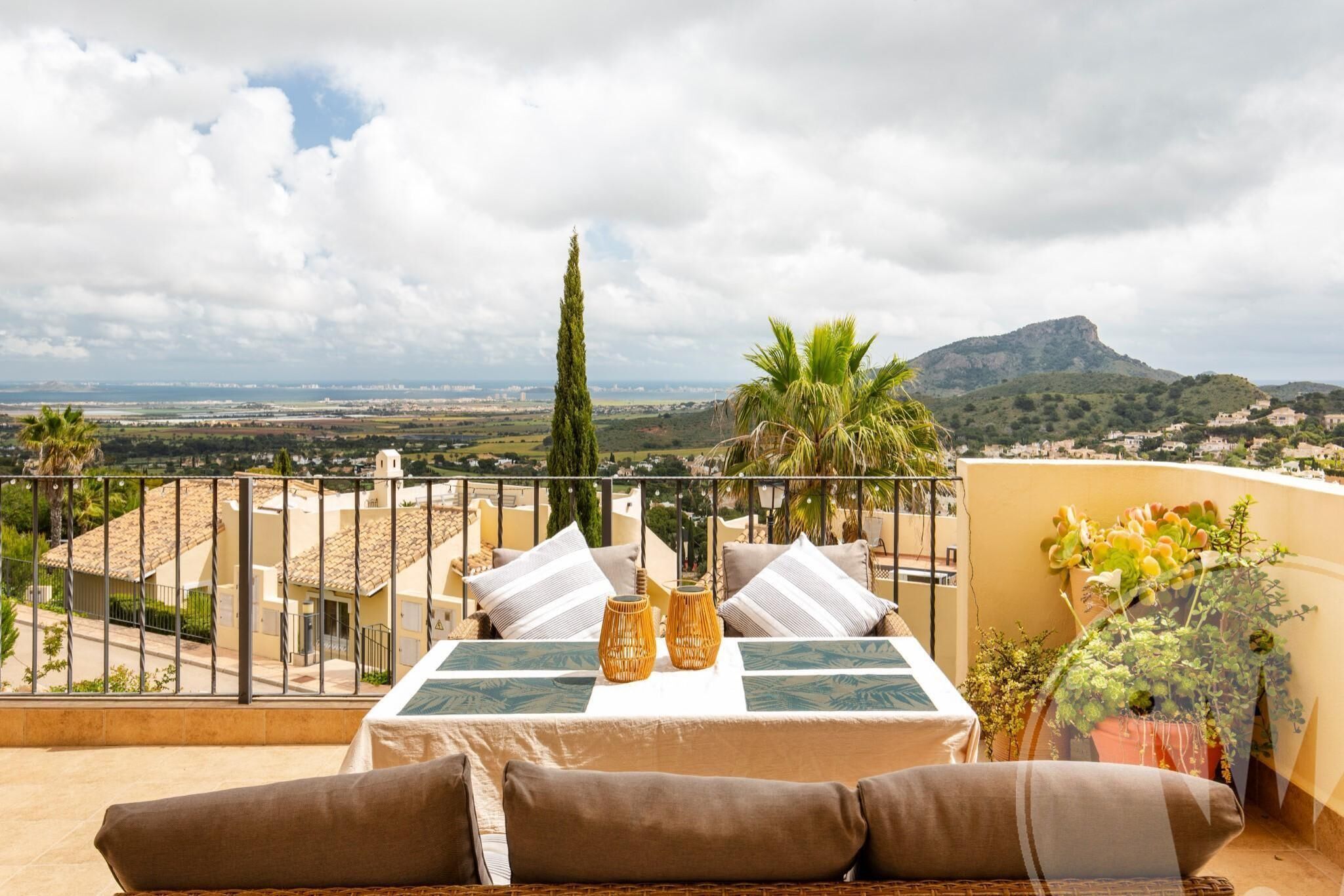 Ein Balkon mit Tisch, Kissen und Topfpflanzen.